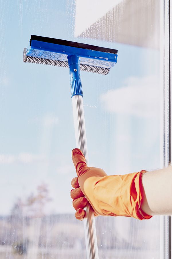 Behandschuhte Hand zieht mit einem Abzieher eine Fensterscheibe ab