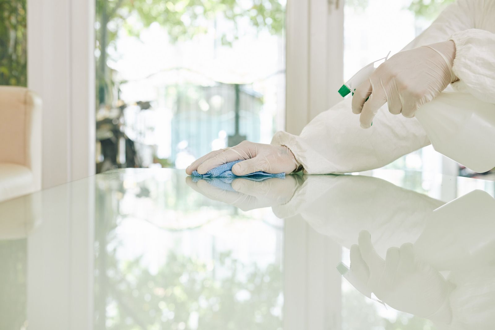 Behandschuhte Hand wischt mit einem blauen Tuch eine Glasfläche